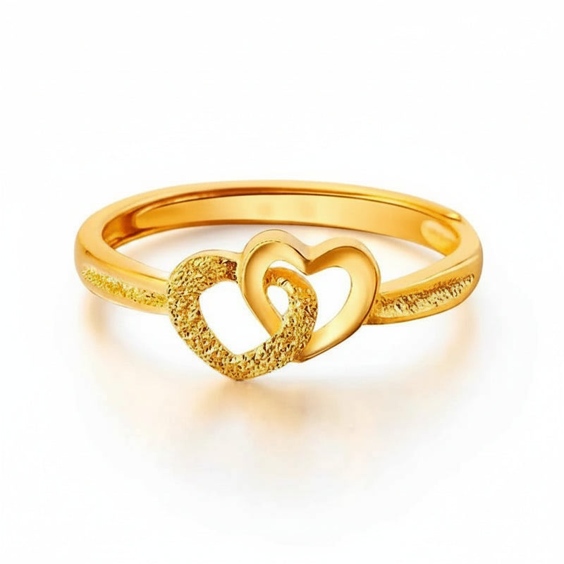 A gold-colored ring featuring two interlocking hearts, with one heart and the ring band finished in a textured, glittery effect and the other heart polished to a smooth shine.