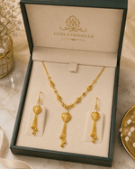 Gold necklace and earrings set in a 'LUXE ÉTERNELLE' box on a marble surface.