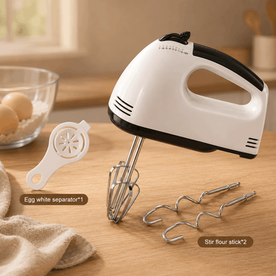 Hand mixer with attachments on a wooden surface, with eggs and a bowl in the background.
