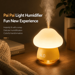 Mushroom-shaped light humidifier emitting steam on a wooden surface with books and a blanket in the background.