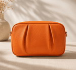 Orange leather bag on a beige surface with a neutral background