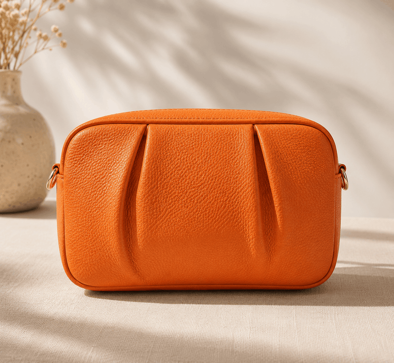Orange leather bag on a beige surface with a neutral background