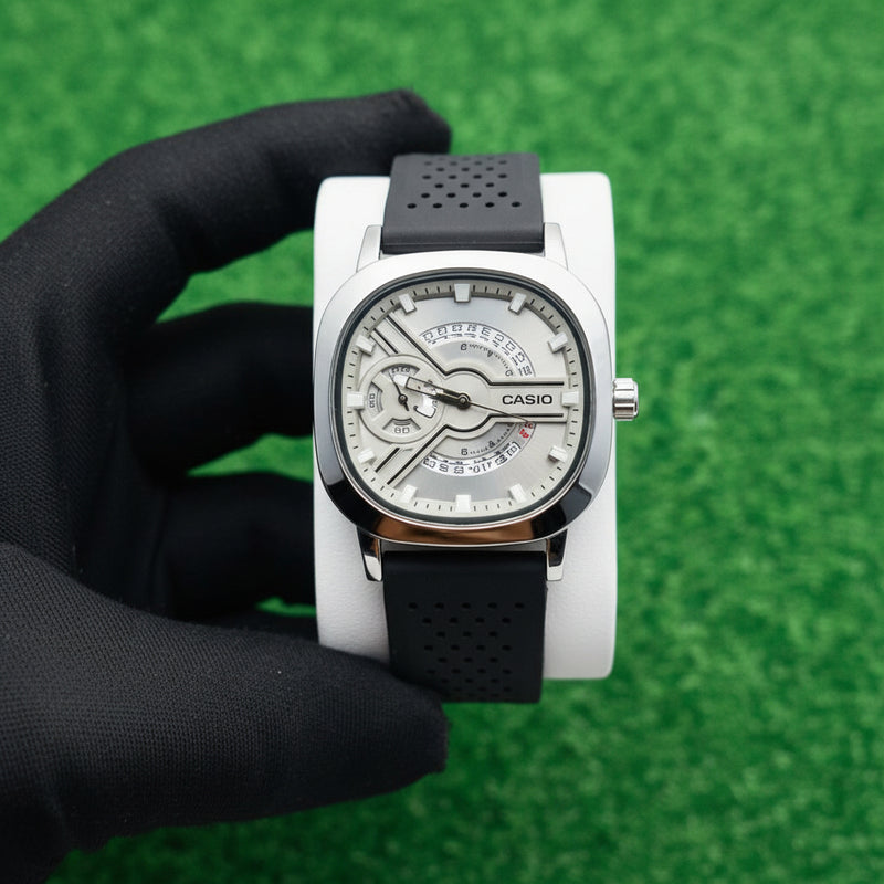 Watch with a black strap held by a hand on a white surface with grass in the background At Aezoon